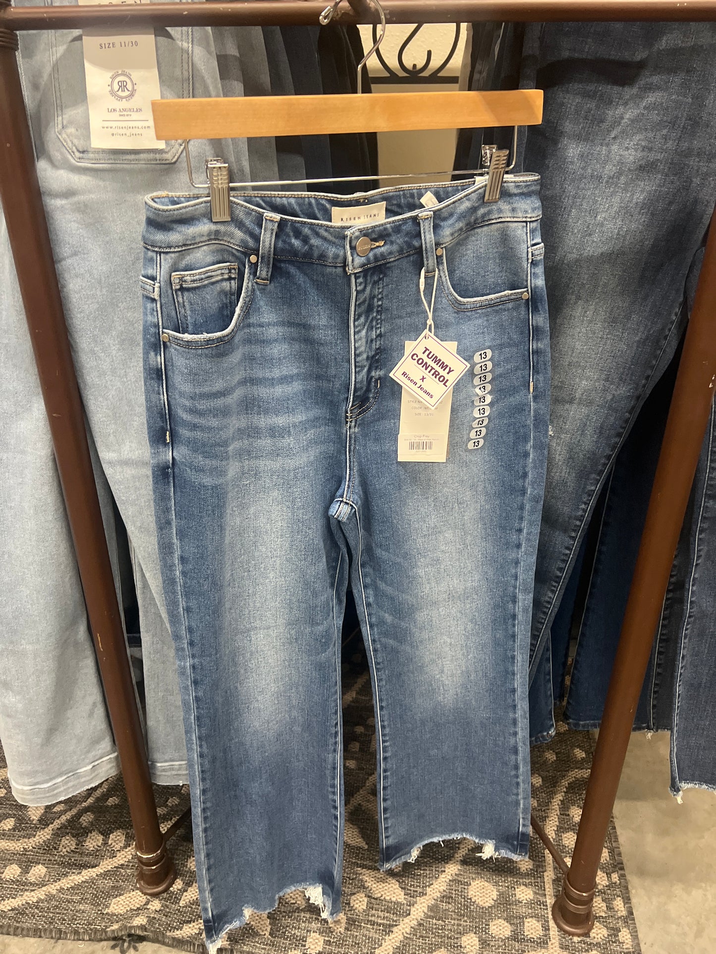 Pair of blue jeans on a hanger with a tag, displayed on a patterned rug.