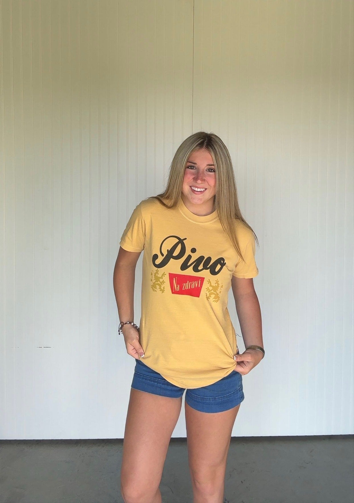 Person wearing a yellow t-shirt with 'Pivo' text and blue shorts against a plain background