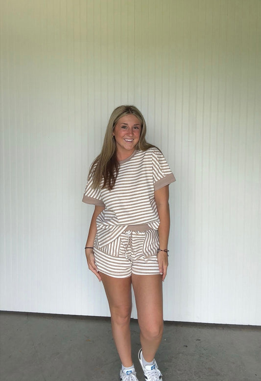 Woman wearing a striped outfit standing against a white wall.